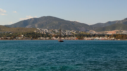 Fototapeta premium Sailboat floating calm turquoise waters Bitez bay, Bodrum, Turkey coastline framed by green mountains