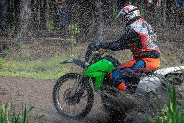Naklejka premium Enduro racer riding splashing puddle of water and mud