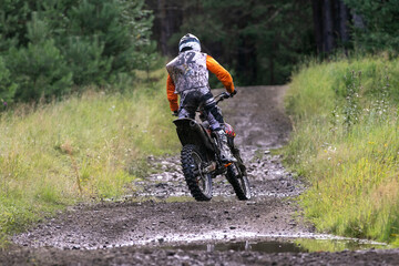 Obraz premium Back enduro racer rides on forest trail through mud and water