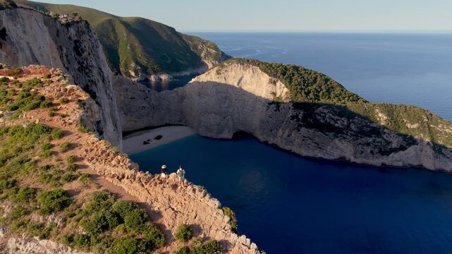 Witness the stunning scenery of Navagio Beach in Zakynthos, Greece, where azure waters meet dramatic cliffs. A couple of men and woman standing on the cliff during vacation