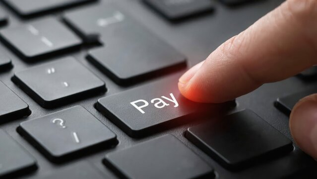 Finger pressing the pay button on a black computer keyboard for online shopping