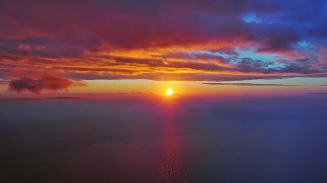 Aerial view of bright sun setting over calm sea. Scenic view of ocean horizon with dramatic clouds. Natural landscape background, 4k