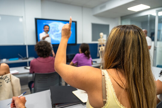 Student raising hand during university lecture in modern classroom