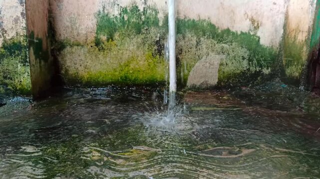 Clear water flowing from a metal pipe into a mossy concrete pool in a rural area