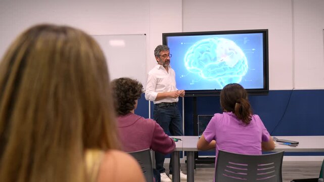 University professor explaining human brain anatomy to a class of attentive medical students during a lecture, pointing at a digital screen displaying a 3d model of the nervous system