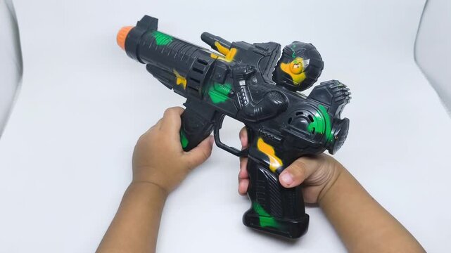 Childs Hands Holding a Futuristic Black Toy Gun with Green and Yellow Accents