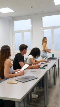 Group of young university students handing in their final exam papers to the professor one by one and happily leaving the classroom as the school year concludes