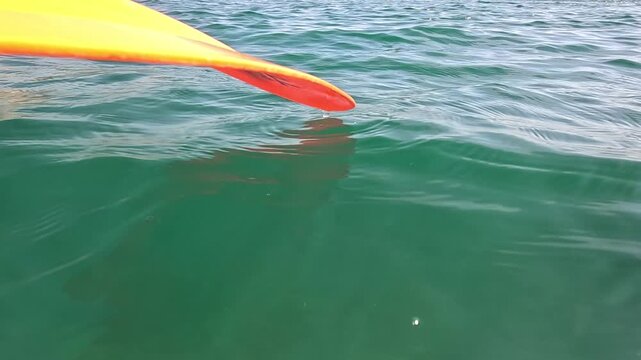 Kayak paddle ocean close up of an orange paddle blade dripping water into turquoise sea waves during a peaceful summer vacation