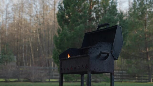 Outdoor charcoal grill smoking in a backyard garden near a house