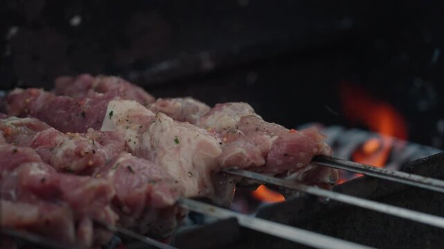 Fresh marinated meat grilling on metal skewers over hot charcoal and open flame