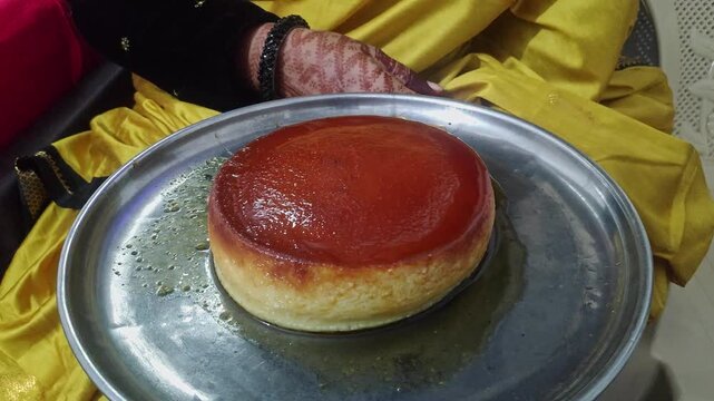A video of an Indian saree-clad woman holding a caramel flan dessert, showing its smooth texture