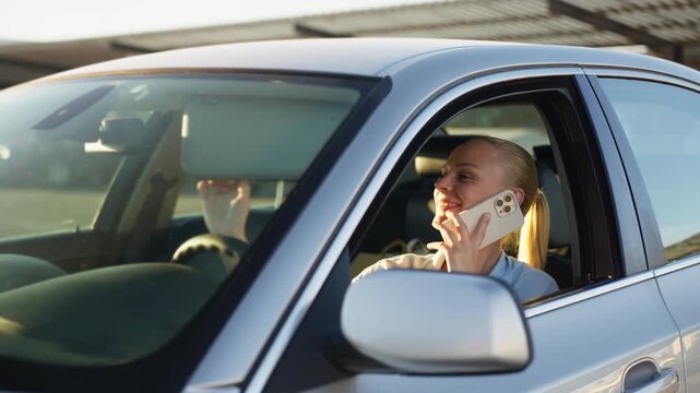 Relaxed woman sitting in parked car and talking on smartphone, enjoying quiet break and friendly conversation during everyday routine.Taking break, waiting, everyday lifestyle concept