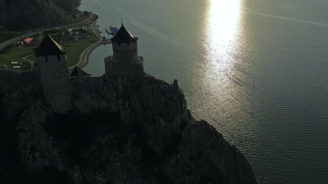 Aerial around view of Golubac medieval fortress on cliff above Danube river at sunset, historic landmark in Serbia, 4k