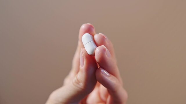 White oval pill held by woman fingers close up on beige background highlighting vitamin support concept. Nutritional supplementation, nutrient intake and wellness maintenance for healthy lifestyle