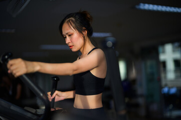 Fototapeta premium A focused young woman in workout attire exercises intensely on a gym machine in a dimly lit fitness center.