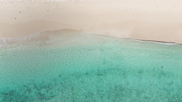 Top down minimalist aerial drone view over calm transparent turquoise sea ripples washing onto the clean white sandy shore of St Lawrence Gap beach in Bridgetown, Barbados.