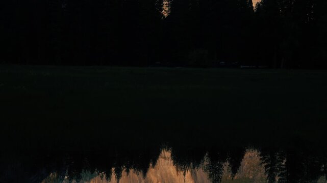 Tilt up of Half Dome reflected in Merced river near sunset with alpenglow on the rock in Yosemite National Park, California.