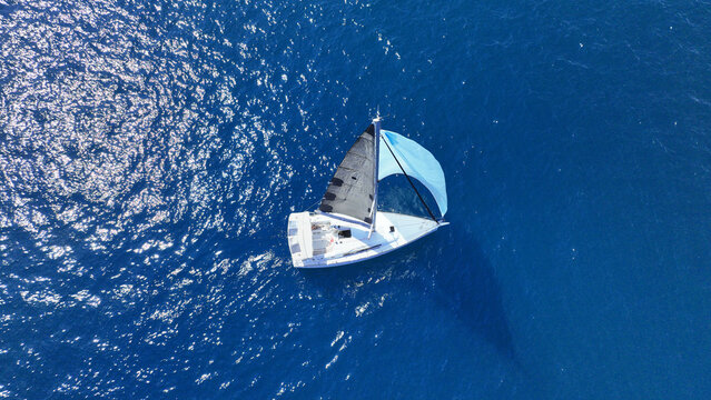 Aerial drone photo of small sail boat with blue sails cruising in deep blue Mediterranean Sea