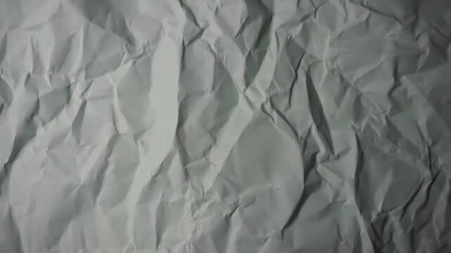 Close-up video showing the texture of a crumpled and creased piece of white paper. Ideal for abstract backgrounds, overlay effects, rough paper textures, creative design projects, and concept videos r