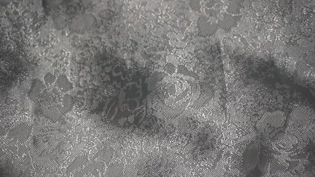 Close-up of silver satin brocard fabric with elegant floral damask pattern and shimmering light effect