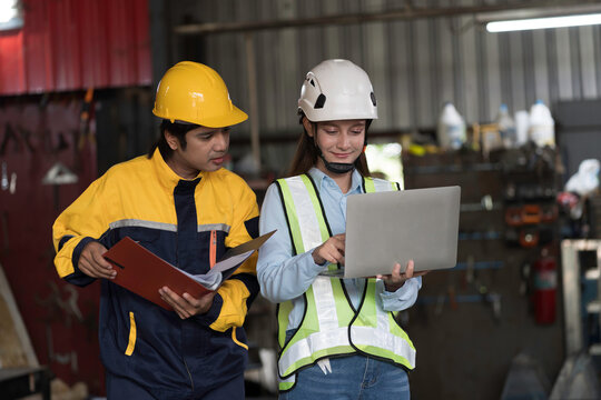 Factory worker working with computer laptop in factory. Male and female engineer wearing safety uniform, helmet discussing at work factory