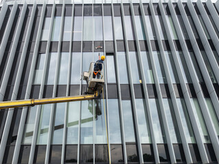 Professional window washer cleaning glass facade of modern office building using cherry picker crane, maintenance worker washing windows on high rise skyscraper © Rokas