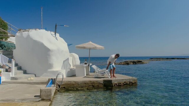 Enjoy the tranquil beauty of Mandrakia Milos Island in Greece as a men traveler relaxes by the crystal clear waters. Whitewashed buildings reflect the summer sun, creating a perfect holiday escape