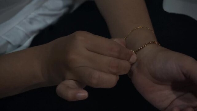 Close up of hands putting on and fastening delicate gold chain bracelet on wrist