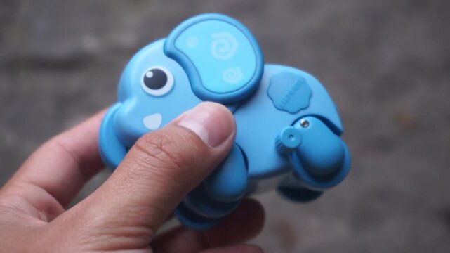 Hand holding a blue plastic wind-up elephant toy outdoors