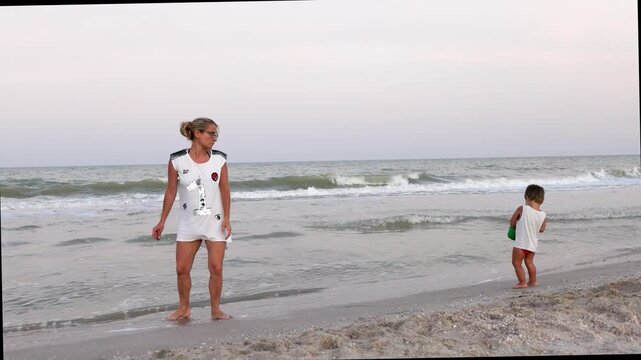 The kid collects shells and pebbles in the sea on a sandy bottom with his mother under the summer sun on vacation