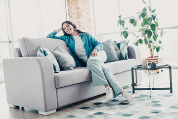 Obraz premium Smiling woman relaxing on a sofa in a bright living room enjoying a comfortable, casual moment at home