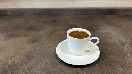 Obraz premium Traditional Turkish coffee in white ceramic cup with saucer on dark textured kitchen countertop, close up high angle view.