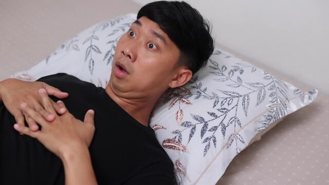 A man lying in bed suddenly wakes up with a startled, shocked expression, looking around anxiously