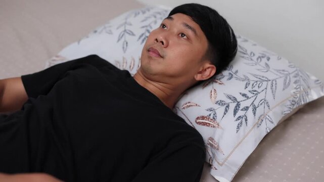 young man lies down on a pillow and pulls up a blanket to sleep