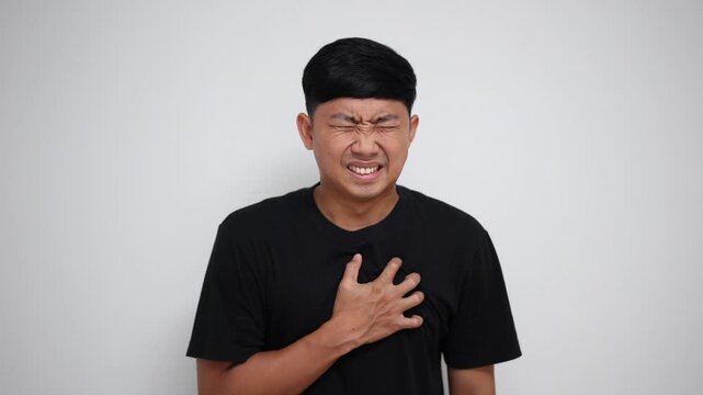 Asian man clutching his chest in severe pain, suffering from a sudden heart attack or stroke