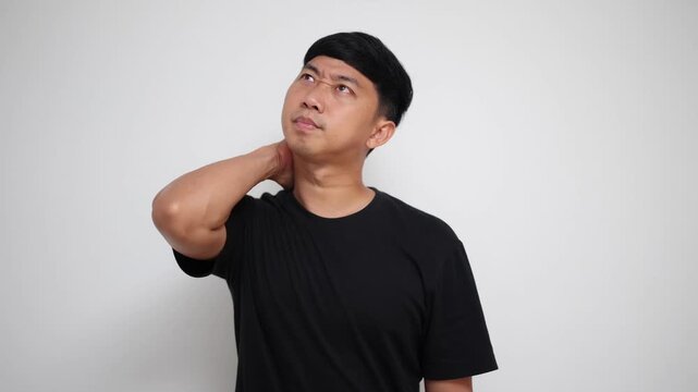 Asian man suffers from severe neck pain and muscle stiffness, massaging himself to find relief