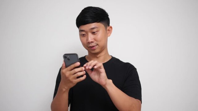 Asian man scrolls through his phone, smiles happily, and excitedly points at the screen