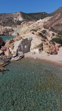 A couple of men and woman walks at the Tsigrado Beach, Milos, Greece captivates with its crystal-clear waters and stunning rock formations. Time stands still as waves gently lap against the shore
