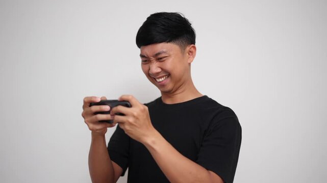 An energetic young Asian man intently playing a fast-paced game on his mobile phone with expressions