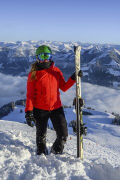 Skier with ski helmet and skis standing at the ski slope, looking into the camera, mountain panorama in the back, SkiWelt Wilder Kaiser, Brixen im Thale, Tyrol, Austria