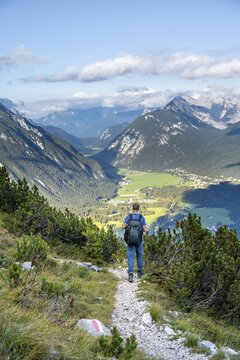 Hiker on hiking trail, in the background valley with village Leutasch and summit of Arnplattenspitze, descent from Hohe Munde, Mieminger Kette, Tyrol, Austria
