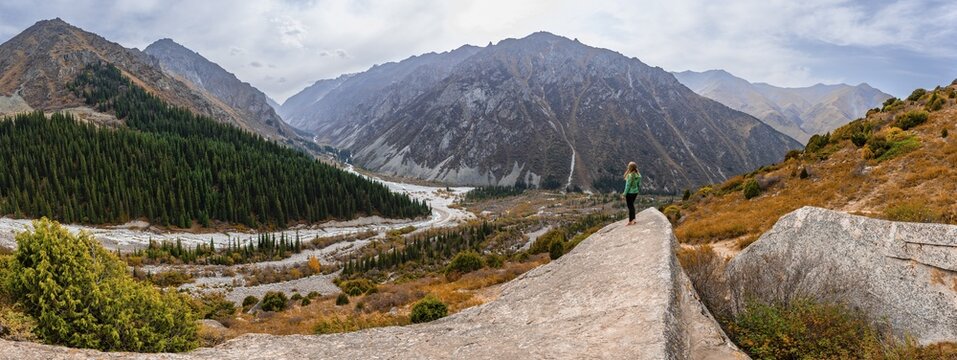 Panorama, view of the Ala Archa valley from the viewpoint, hiker on a large rock, Broken Heart Rock, autumnal mountain landscape, Ak Say and Ala Archa mountain streams, Ala Archa National Park, Khirgiz Ala-Too Mountains, Chuy region, Kyrgyzstan
