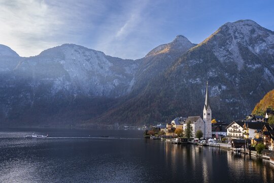 View of Hallstatt and Lake Hallstatt as well as the surrounding mountains. A boat on the lake. In the morning in autumn. Good weather, blue sky. Hallstatt, Gmunden, Salzkammergut, Upper Austria, Austria