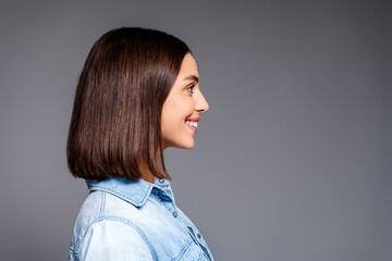 Smiling young woman portrait in profile wearing denim shirt against gray studio background, side view of happy brunette with bob haircut and natural makeup © deagreez