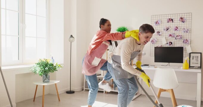 Couple cleaning, vacuuming and dusting the apartment. Wearing aprons and gloves, they share tasks in a tidy bright workspace, using a vacuum, spray, and mop. Teamwork for a tidy home always.