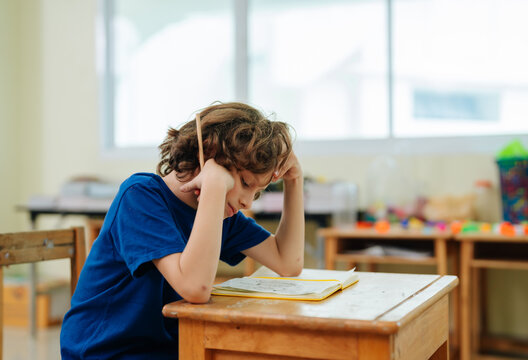 Bored student boy leaning head on hands during school lesson in classroom setting experiencing lack of interest and academic exhaustion within educational environment