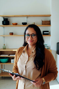 Portrait of young adult Asian businesswoman holding clipboard and smiling at camera in office, presenting professional confidence. Ideal for HR, leadership, recruitment branding, vertical