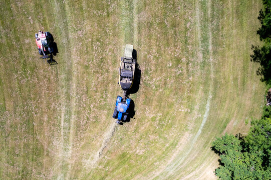 Aerial view of tractors harvesting hay in a green field with mown patterns and nearby trees in Chavannaz, Auvergne-Rhone-Alpes, France.