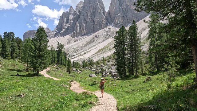 Stunning footage of a woman hiking along the famous Adolf Munkel Trail, framed by the dramatic rocky peaks of the Odle mountain range in the heart of the Dolomites, South Tyrol, Italy.