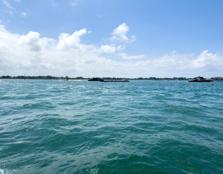 Turquoise sea at Tanjung Benoa beach in Bali, Indonesia, with boats on water, distant shoreline, and blue sky with white clouds.
